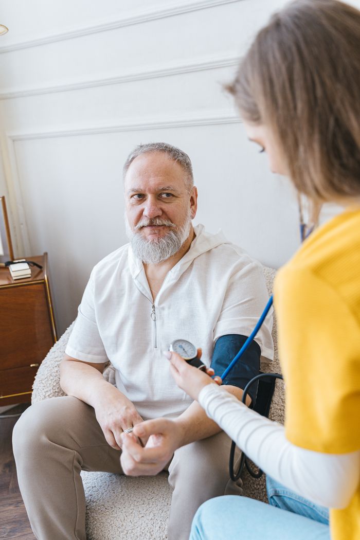 Home A healthcare worker takes the blood pressure of an elderly man using a monitor in a cozy indoor setting.